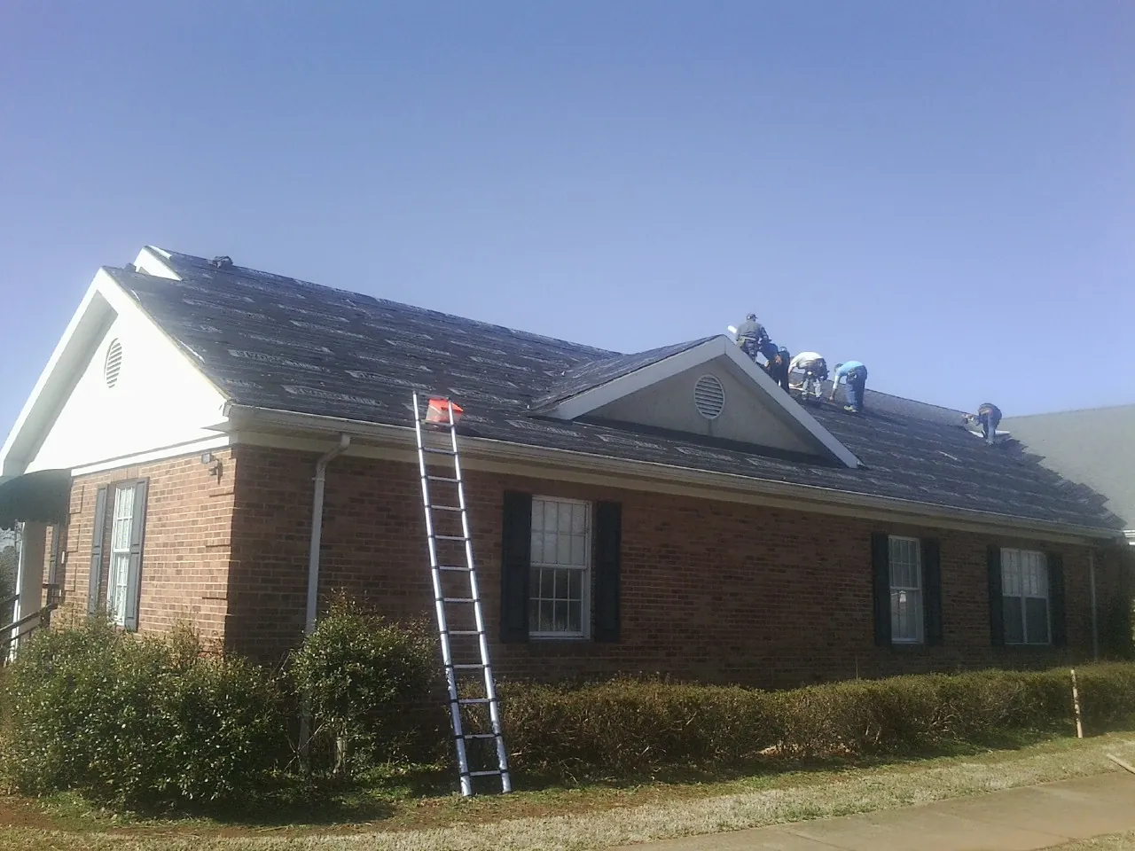Crew tearing shingles off a brick ranch roof with a ladder set — Metal Roof Repair work by our crew in Gibsonia