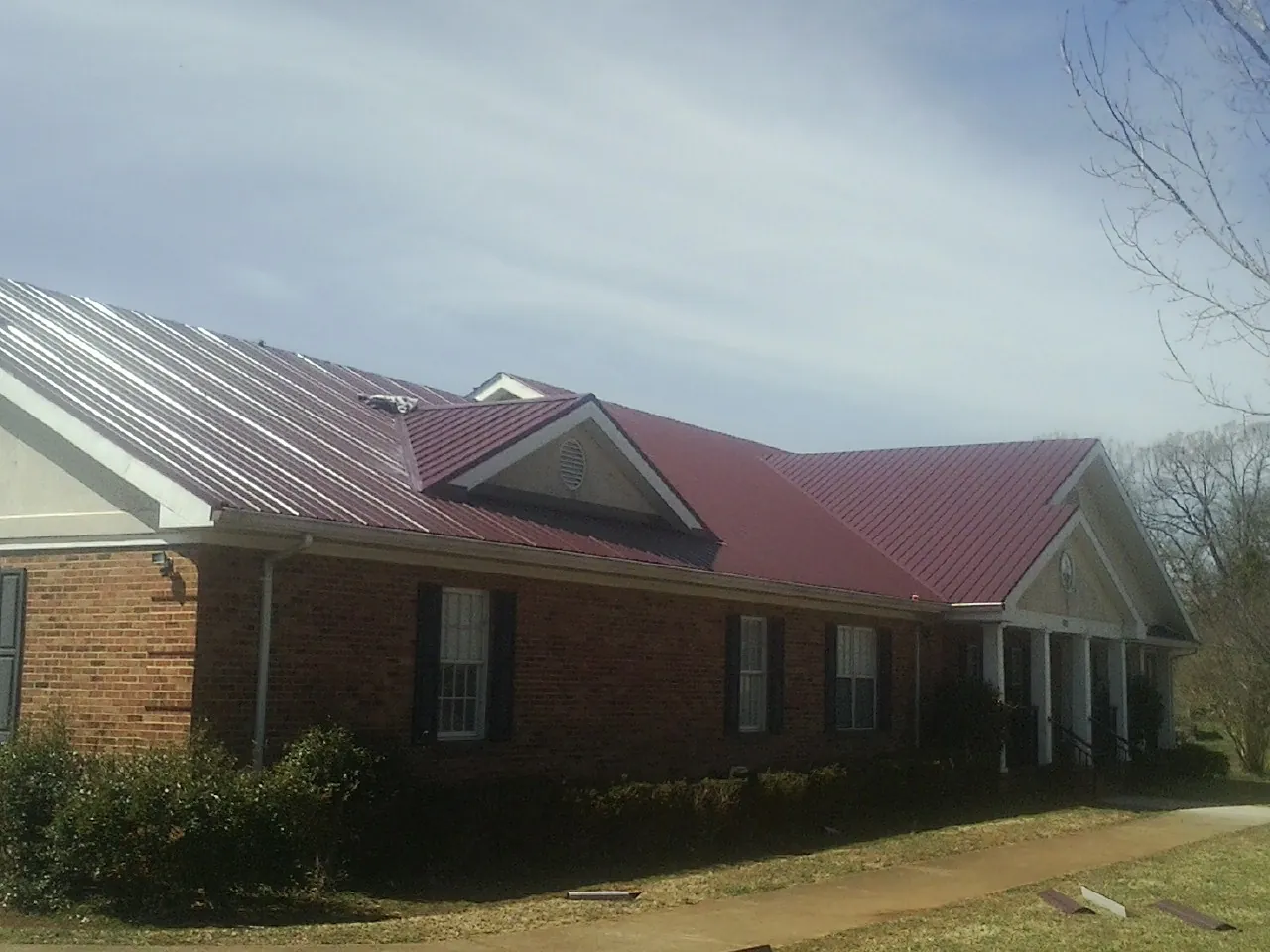 Red metal roof with gabled entries on a long brick building, from a Hail Damage Roof Repair job in Gibsonia