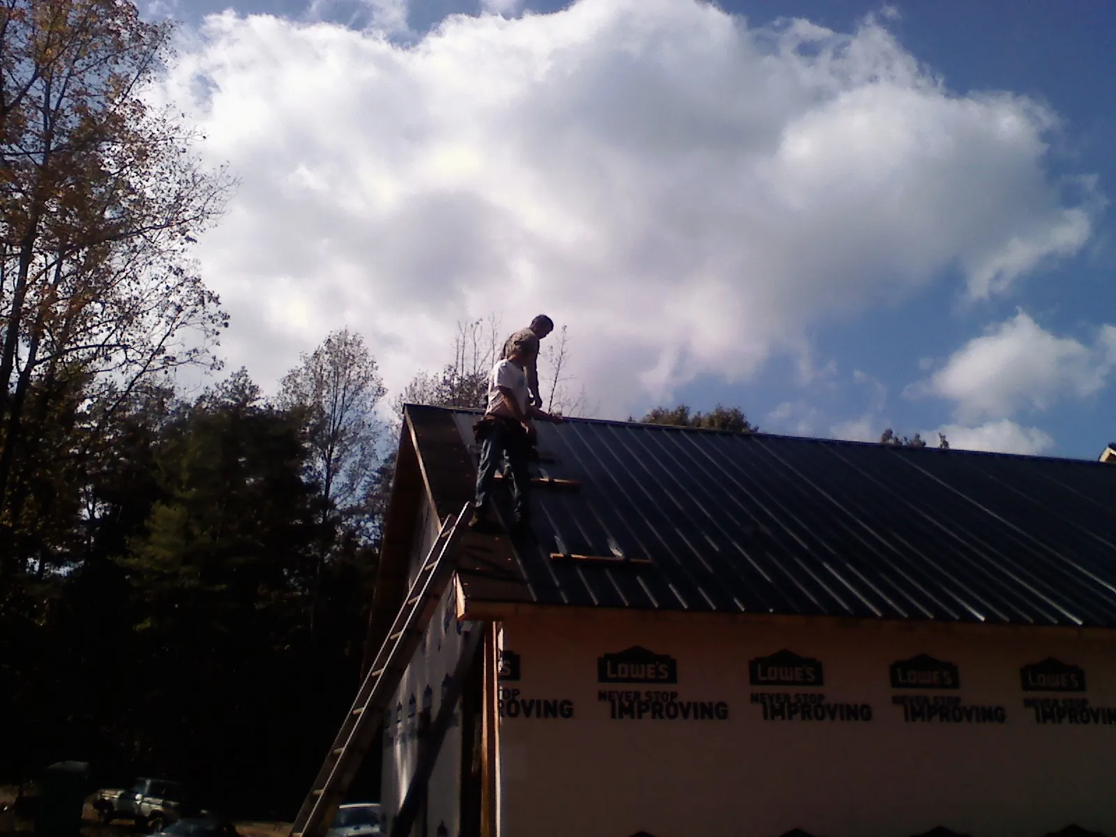 Roofer fastening dark metal panels high against a cloudy sky, from a Roof Inspection job in Gibsonia