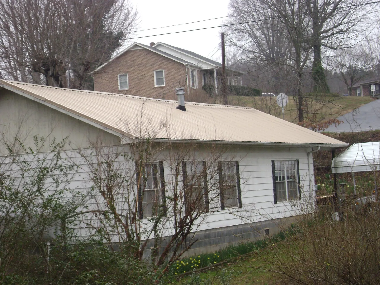 Tan metal roof on a white sided house set into a hillside — Commercial Roofing by Roofing Brothers in Gibsonia